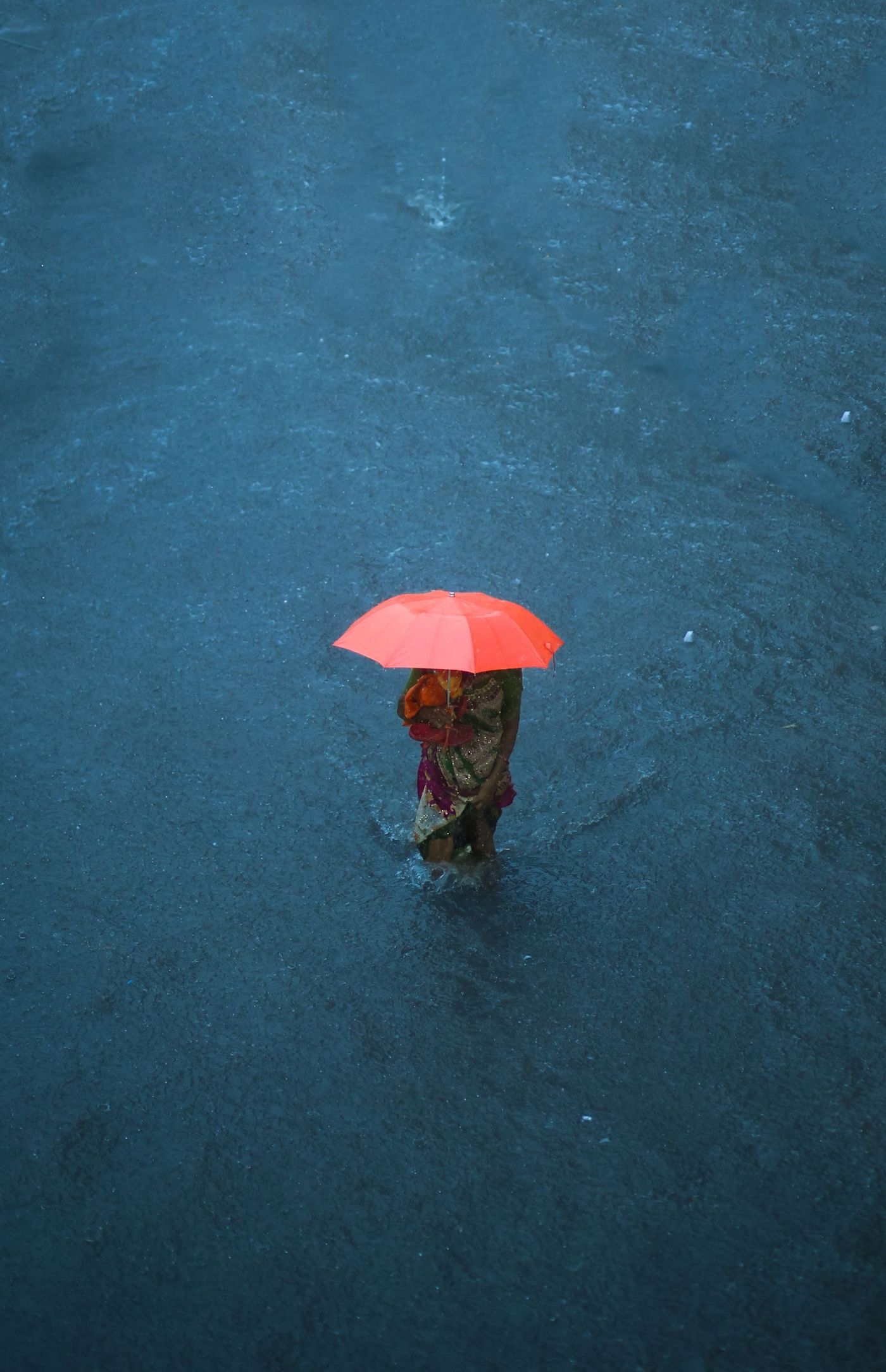 A woman with an umbrella wading through floodwater on a street in India during the monsoon
